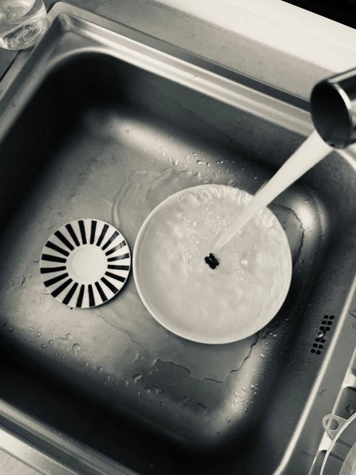 Monochrome view of kitchen sink with dishes being washed under running water.