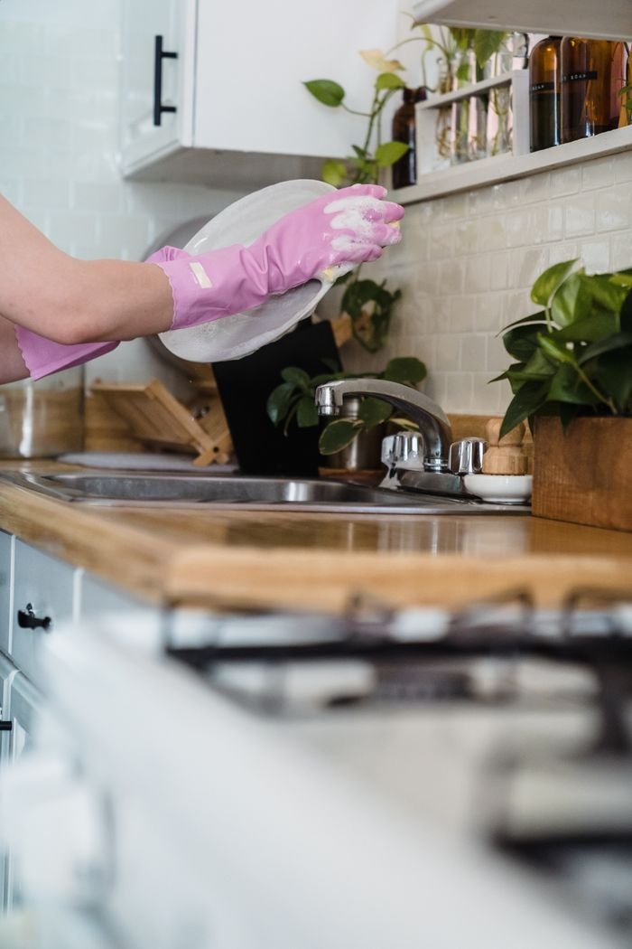 A woman uses pink gloves to wash dishes in a modern kitchen environment.